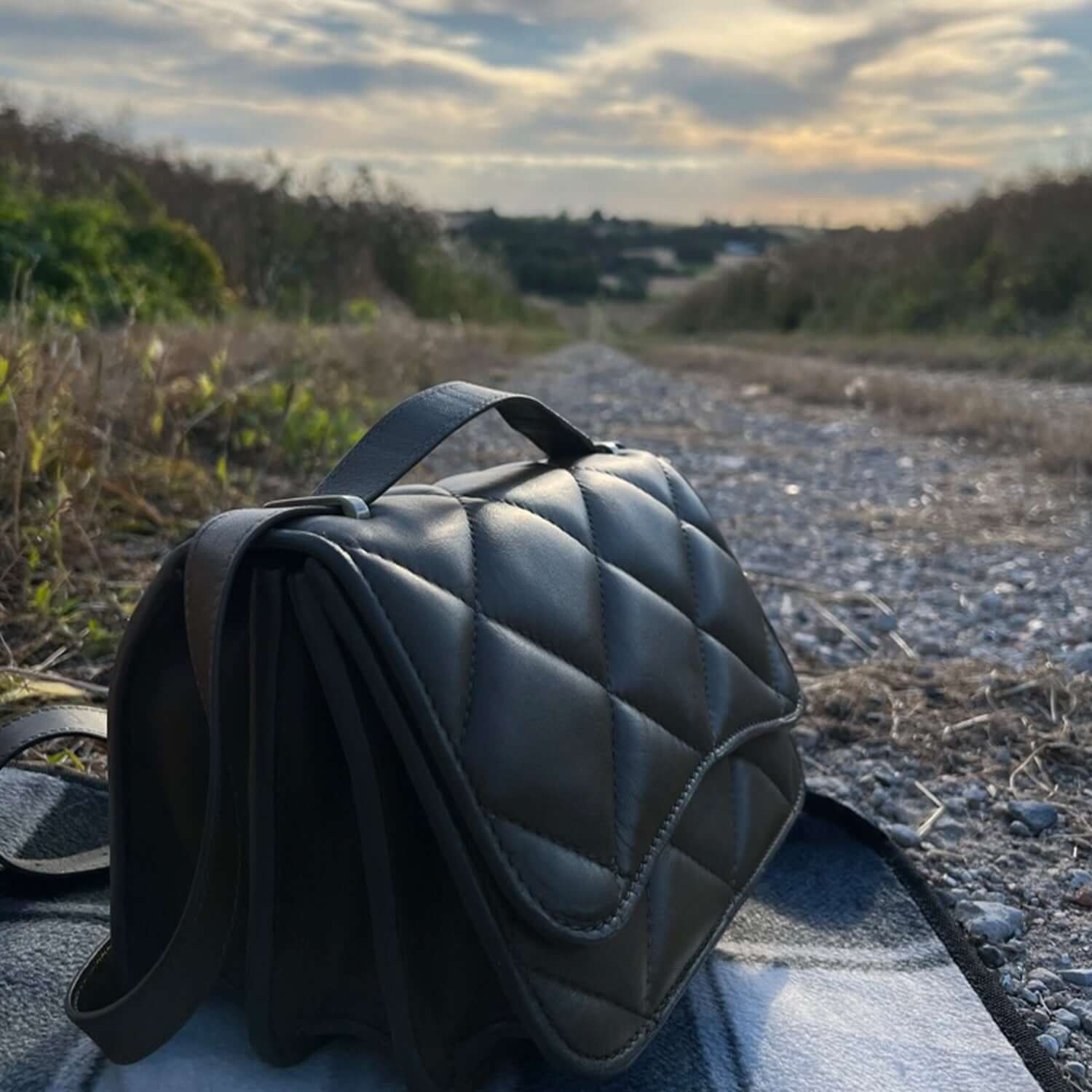 Diamond quilted puffy olive green shoulder bag in open space landscape. Landscape moods - picnic with a view.